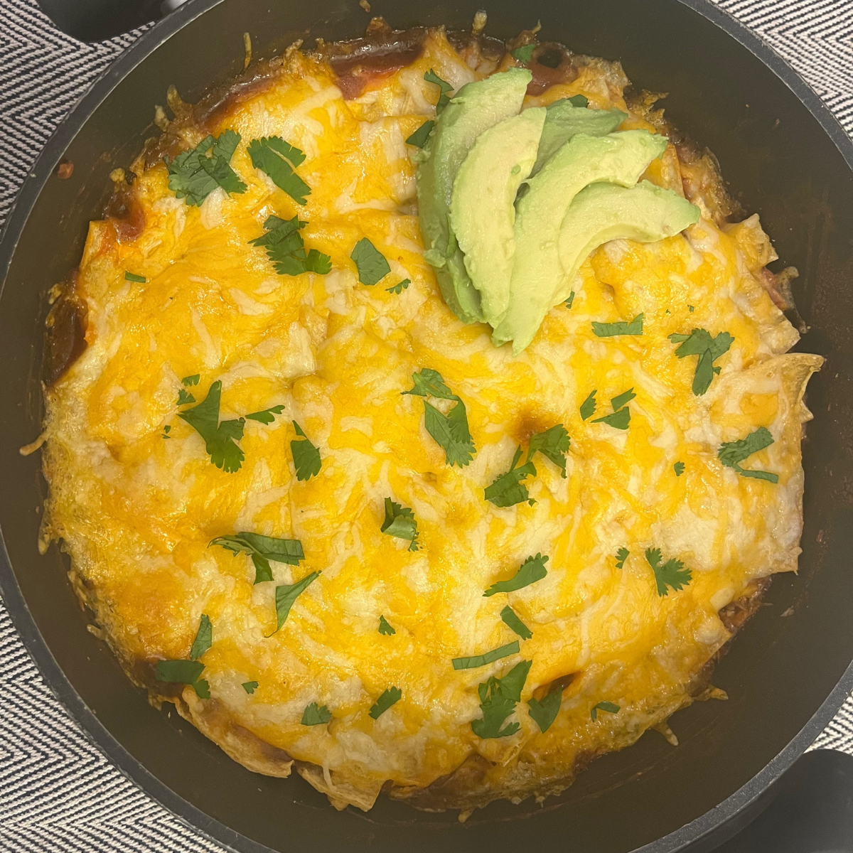 Overhead image of Chicken Enchilada Casserole in a skillet garnished with avocado and cilantro