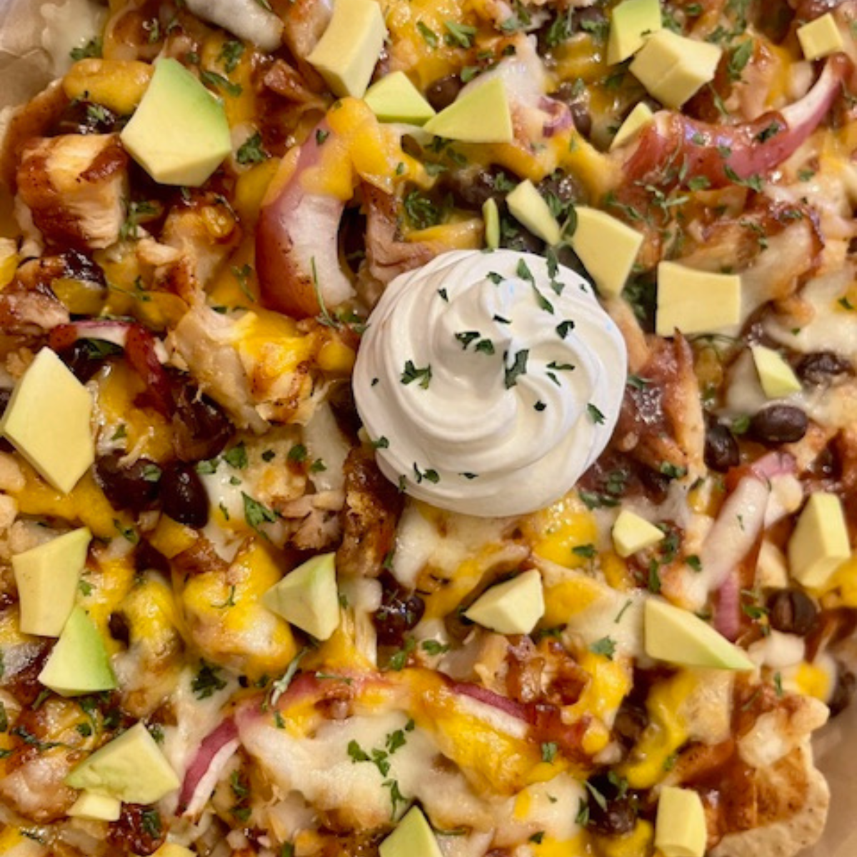 Close up image of BBQ Chicken Nachos with a dollop of sour cream