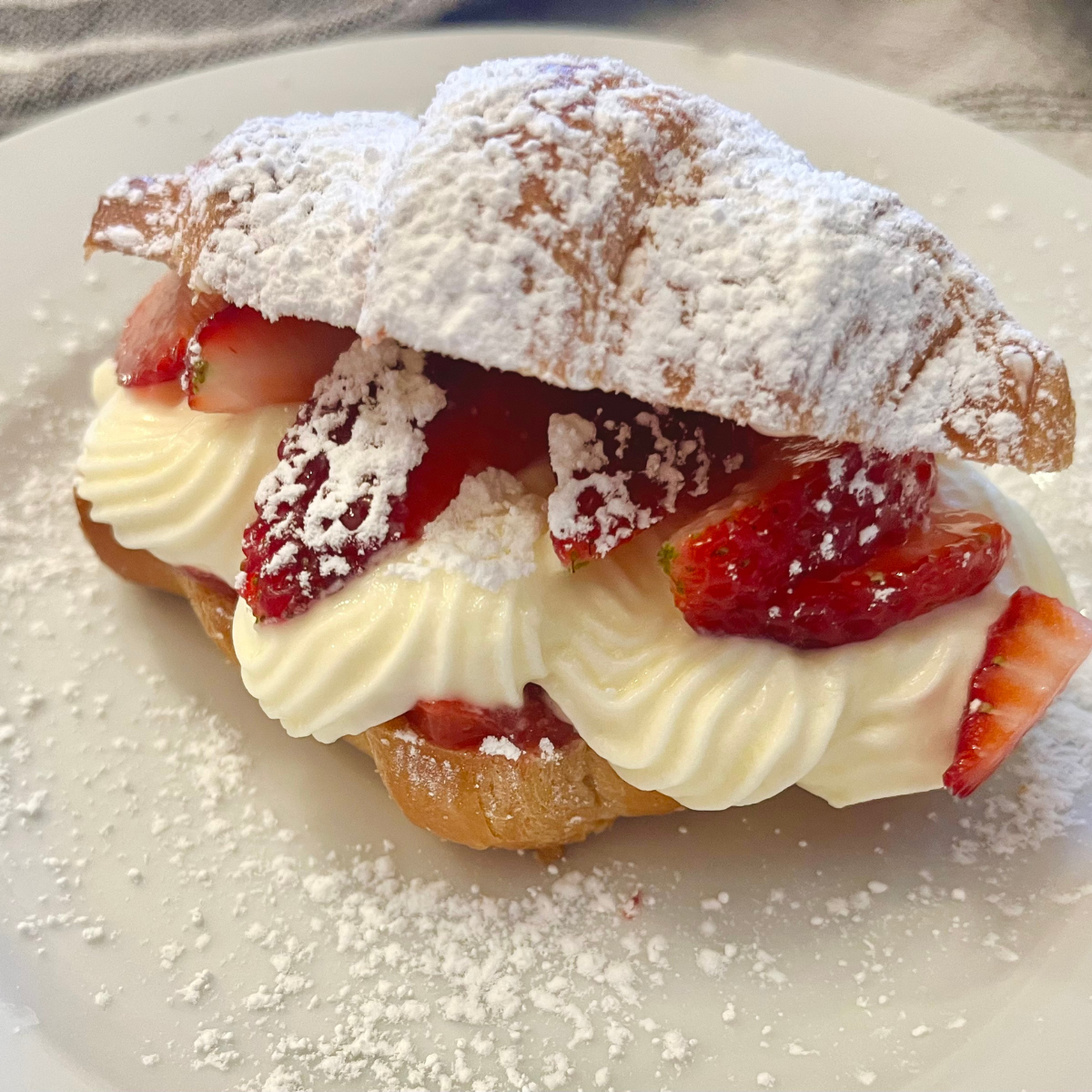 A Strawberry Croissant with cream filling on a white plate