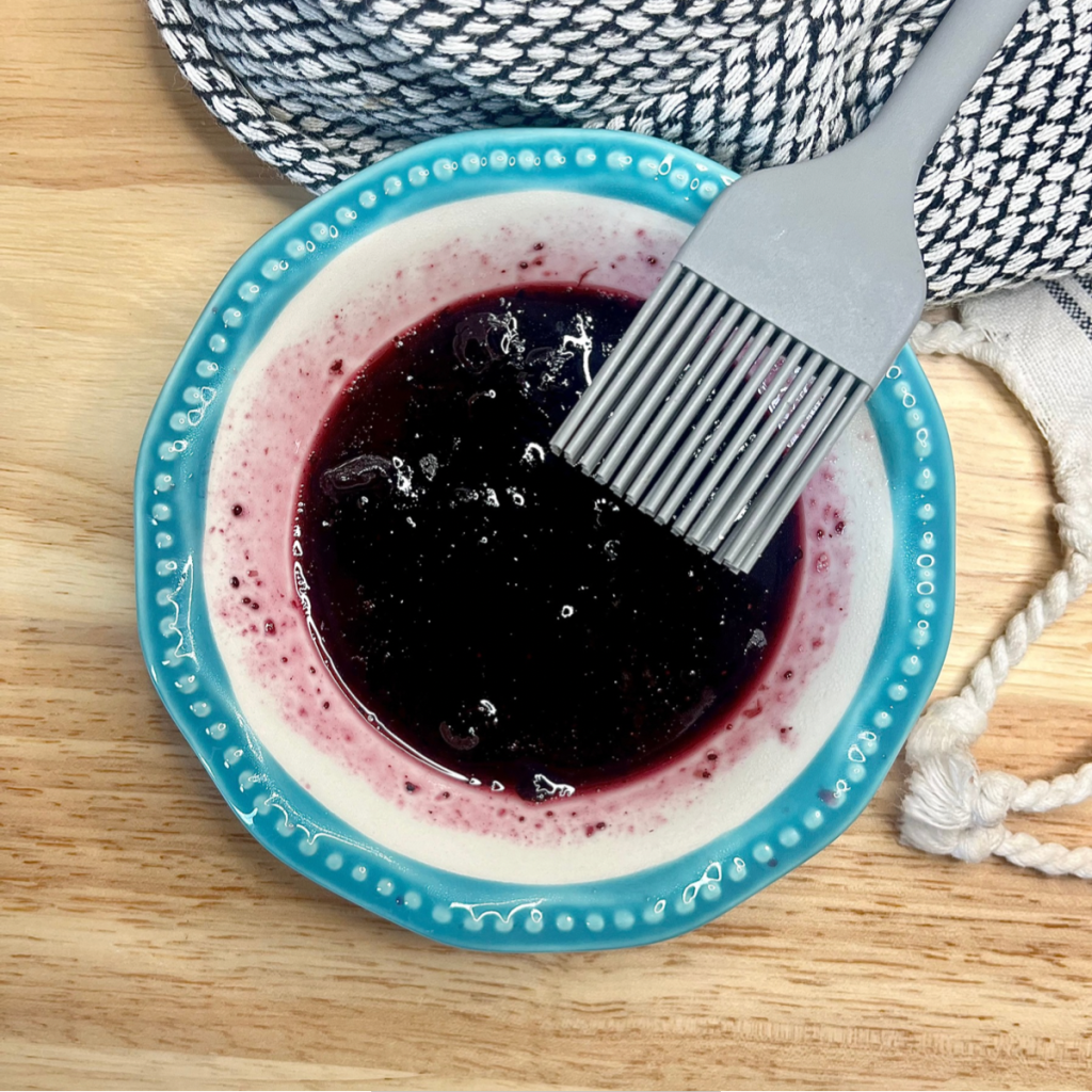 Warmed blueberry preserves in a bowl with a basting brush inside