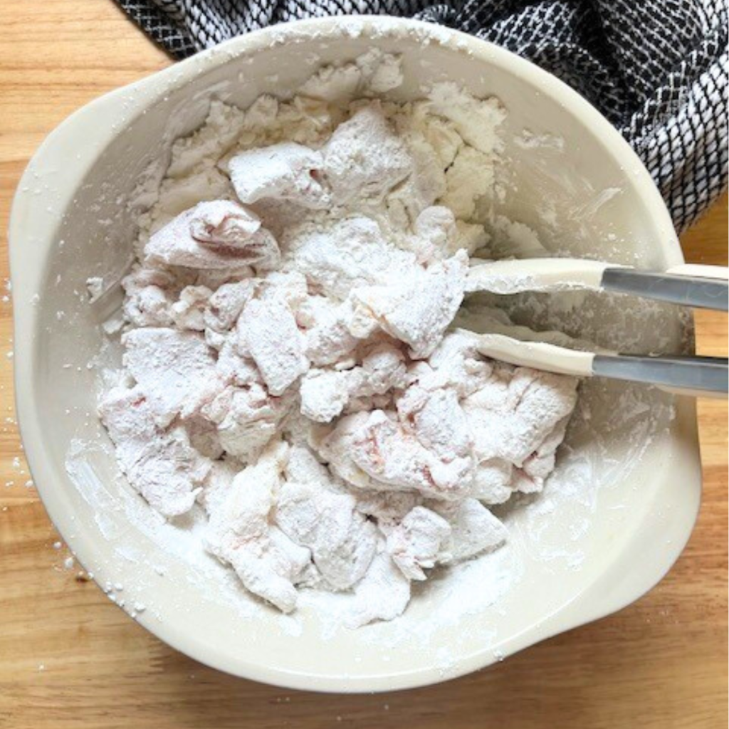 Chicken thigh pieces being coated in cornstarch