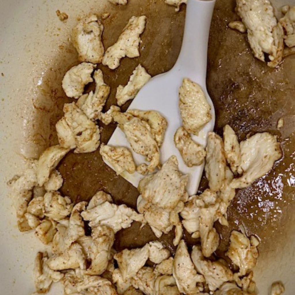Sliced chicken cooked in a skillet with a spatula