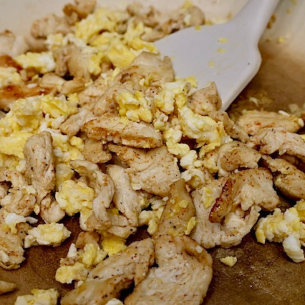 Scrambled eggs and cooked chicken in a skillet with a spatula