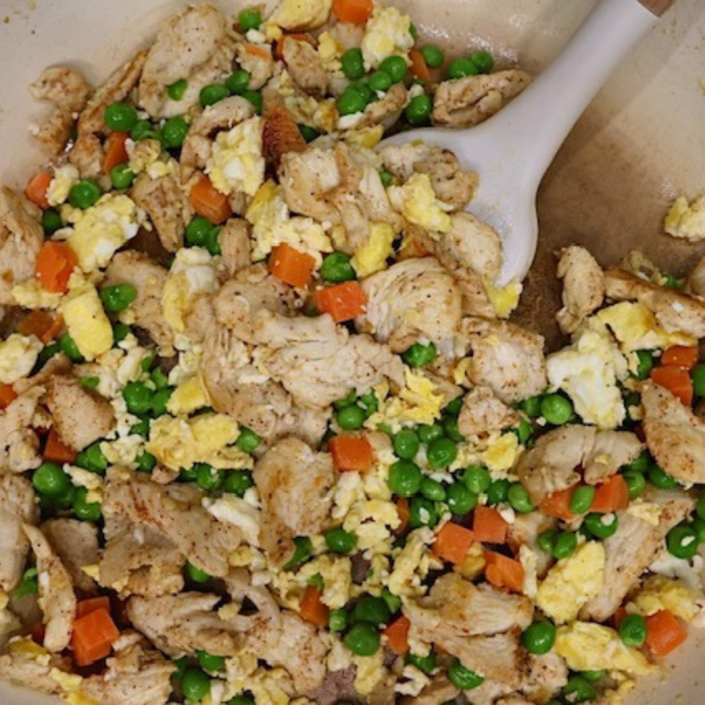 Chicken, scrambled eggs, and mixed veggies in a skillet