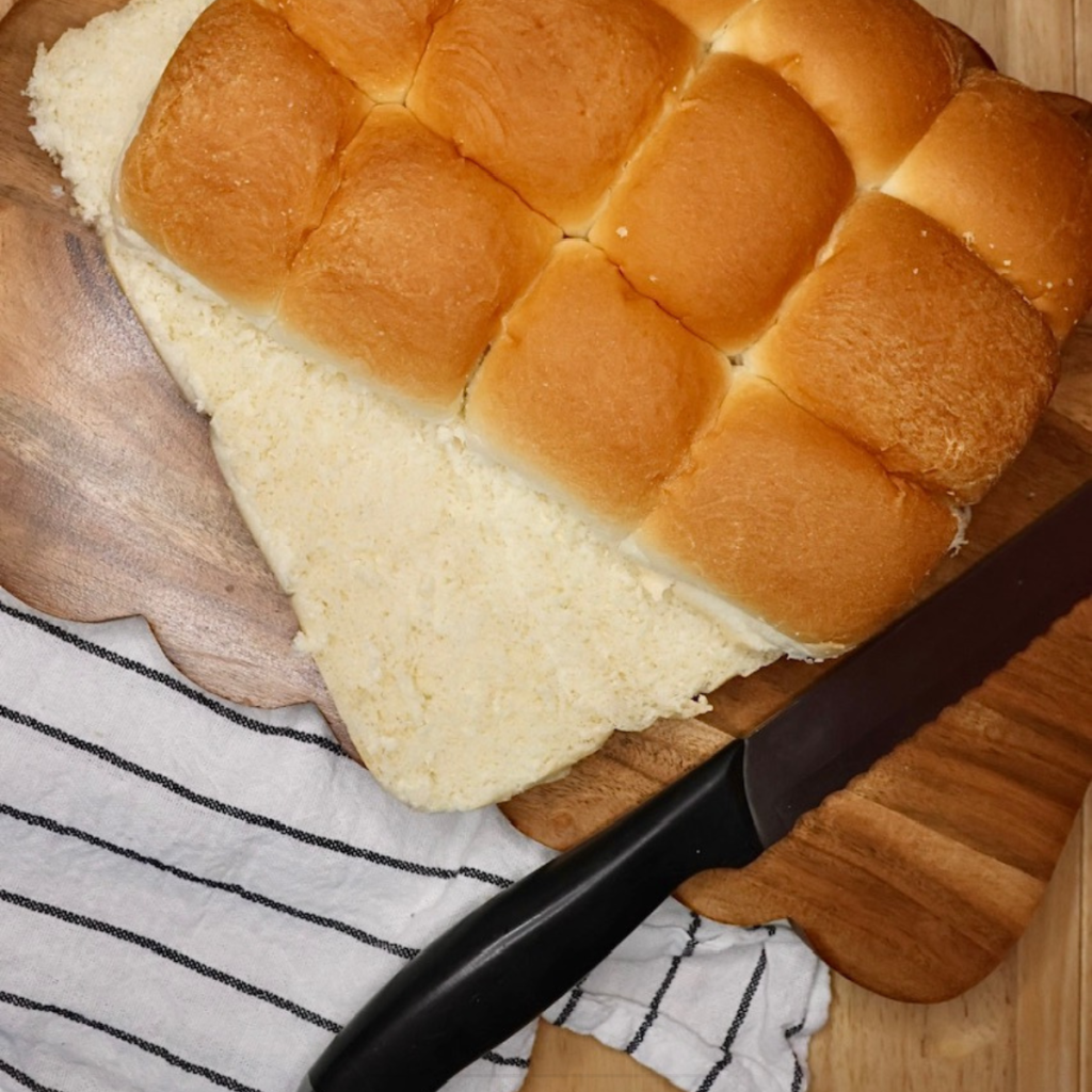 Hawaiian rolls sliced in half horizontally on a cutting board with a knife