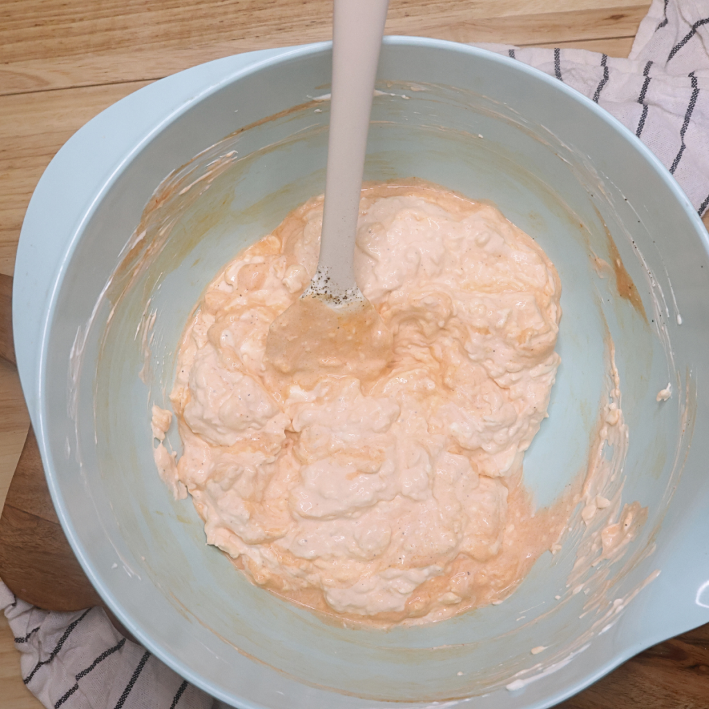 Cream Cheese, sour cream, spices, and buffalo sauce mixted together in a blue bowl