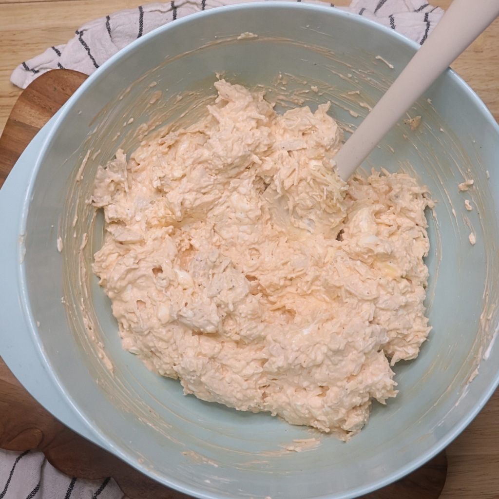 All of the ingredients needed to make baked buffalo chicken dip in a blue bowl