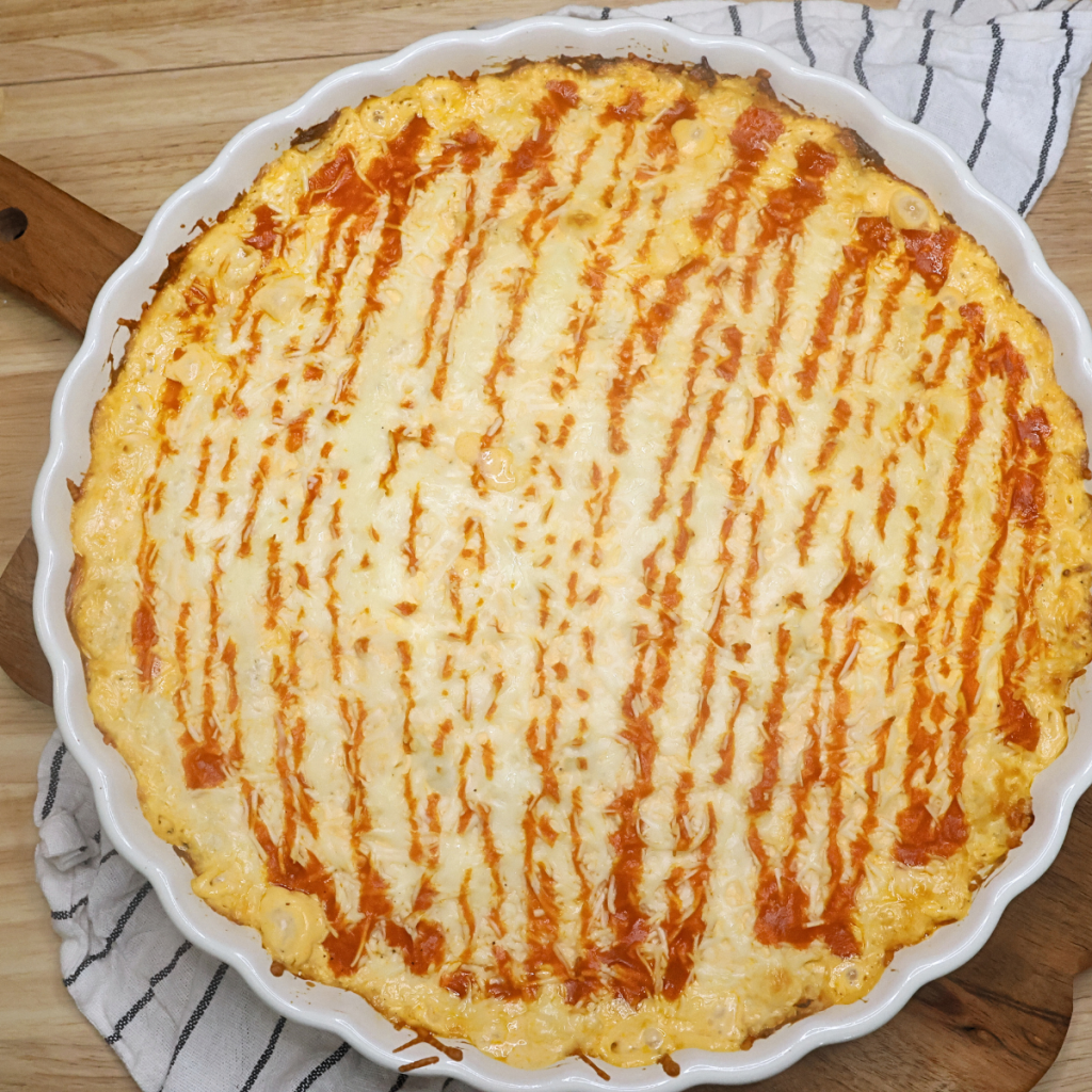 Overhead image of baked buffalo chicken dip in a round baking dish with a drizzle of hot sauce over the top