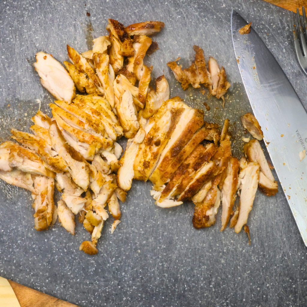 Sliced boneless chicken thighs on a cutting board with a knife