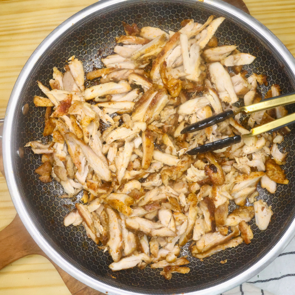 Sliced chicken thighs in a skillet with tongs