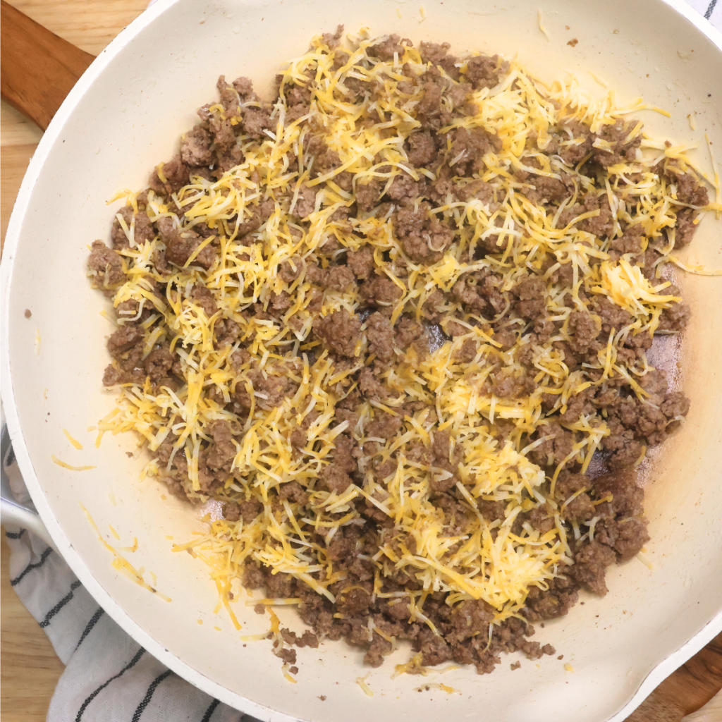 Cooked ground beef with shredded cheese mixed in a skillet