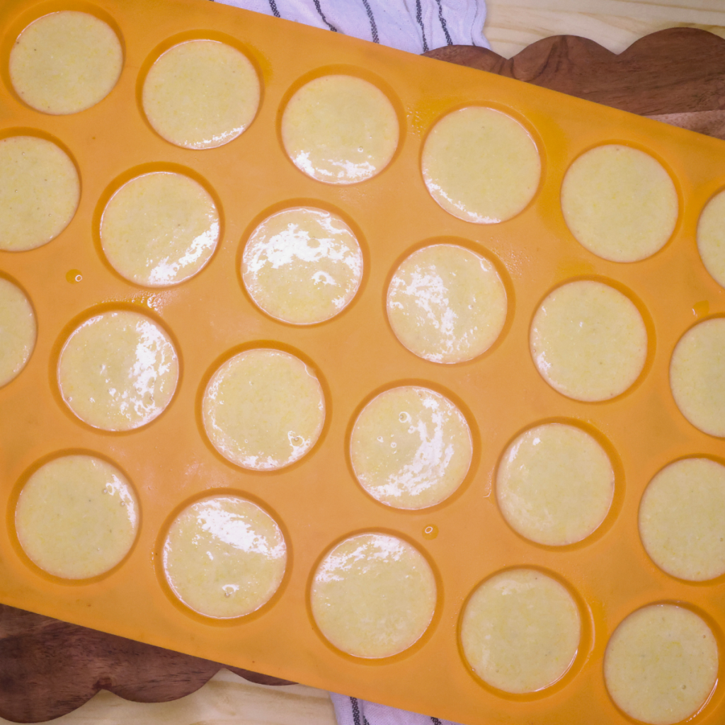 Homemade corn muffin batter in an orange 24 count silicone muffin mould