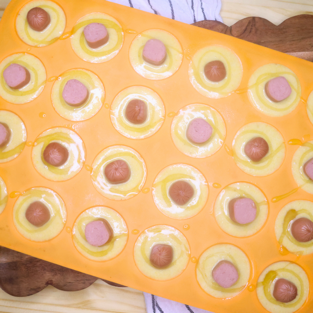 uncooked mini corn dog muffins with honey drizzled on top