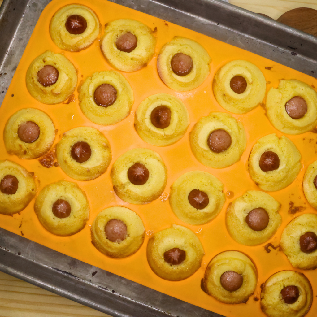 Baked mini corn dog muffins in an orange silicone muffin pan