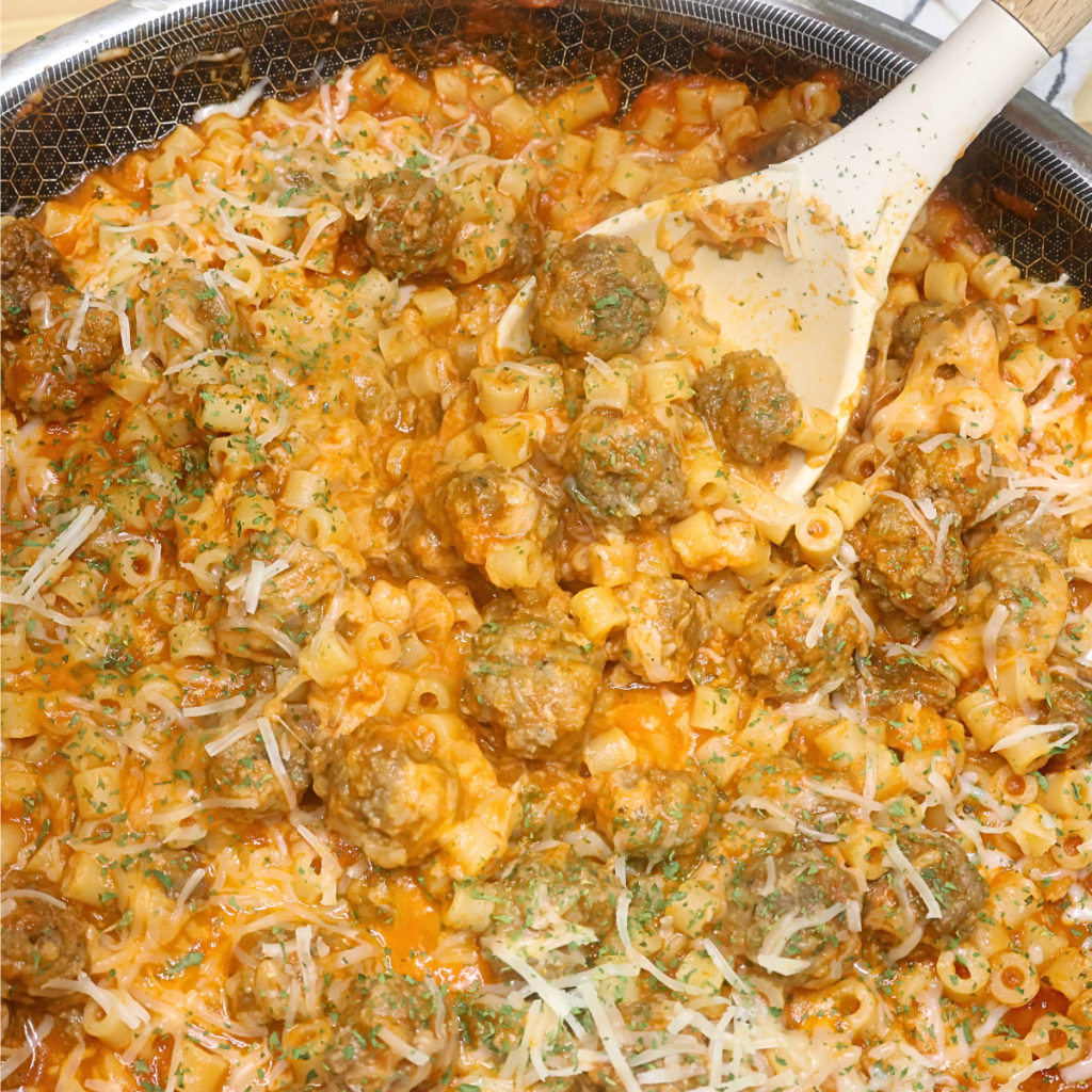 Cheesy ditalini with mini meatballs in a skillet being served with a spoon