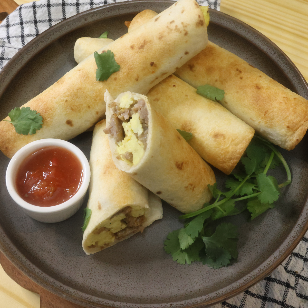 Overhead image of air fryer breakfast taquitos on a plate with cilantro and salsa