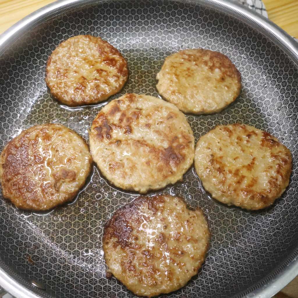 Six sausage patties being cooked in a large skillet
