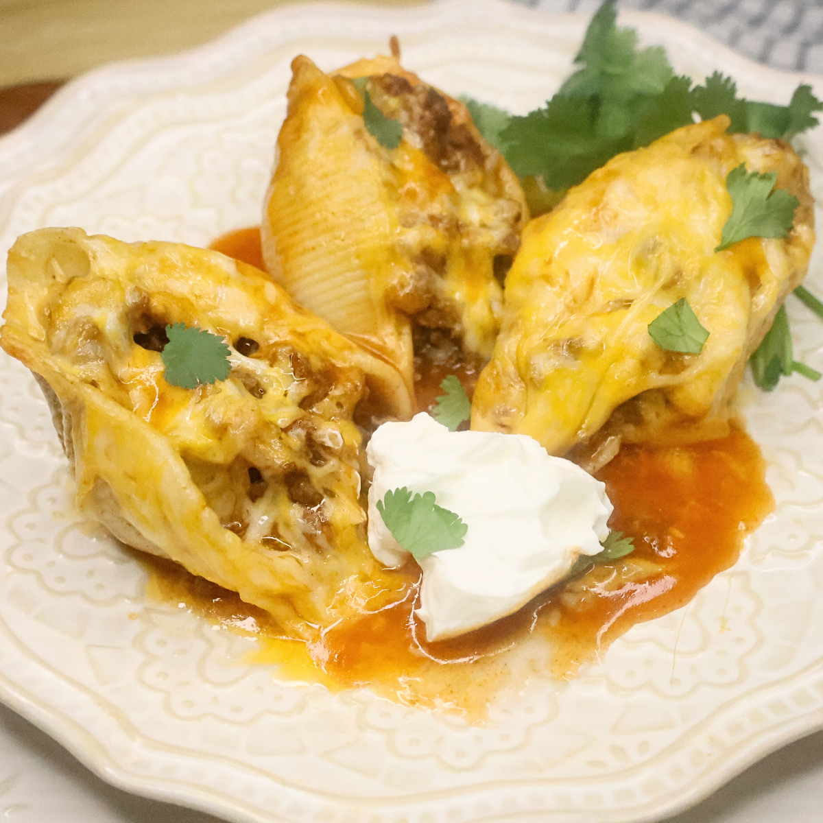 Close up image of three taco stuffed shells with cilantro and sour cream on a plate