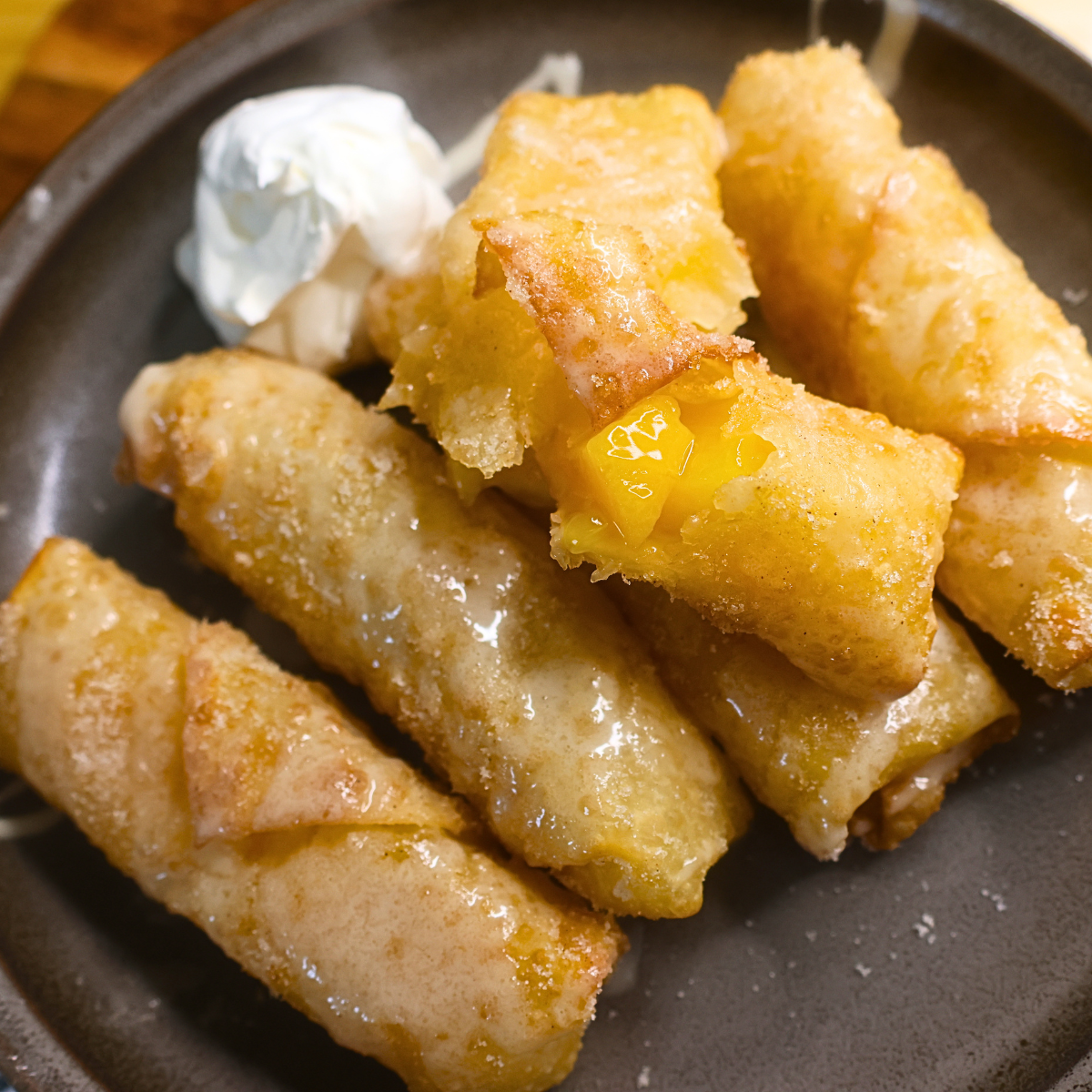 A stack of peach cobbler egg rolls coated in cinnamon sugar and homemade glaze on a plate
