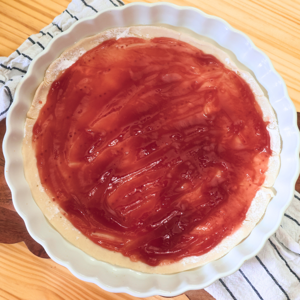 refrigerated pie crust with strawberry jam spread over the top of it in a pie dish