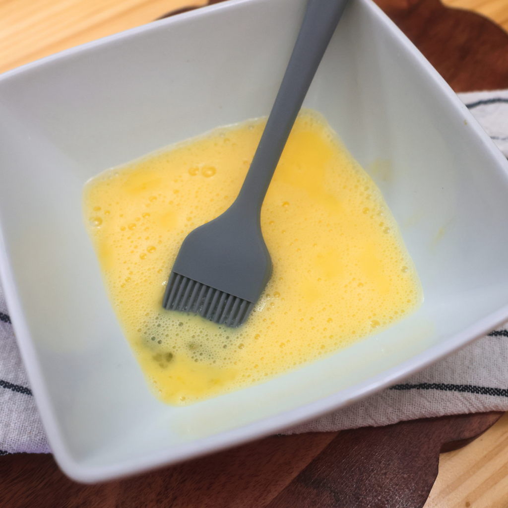 Egg wash in a white bowl with a silicone basting brush