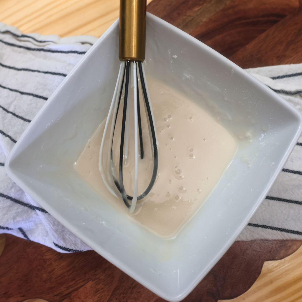 Glaze for a homemade strawberry poptart in a white bowl with a whisk