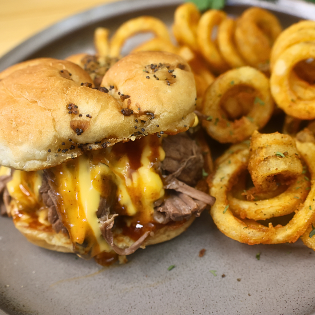 Close up image of a slow cooker pulled beef sandwich with cheddar sauce on a plate with curly fries