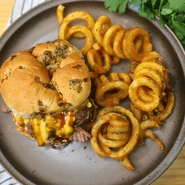 Overhead image of a slow cooker pulled beef sandwich on a plate with curly fries