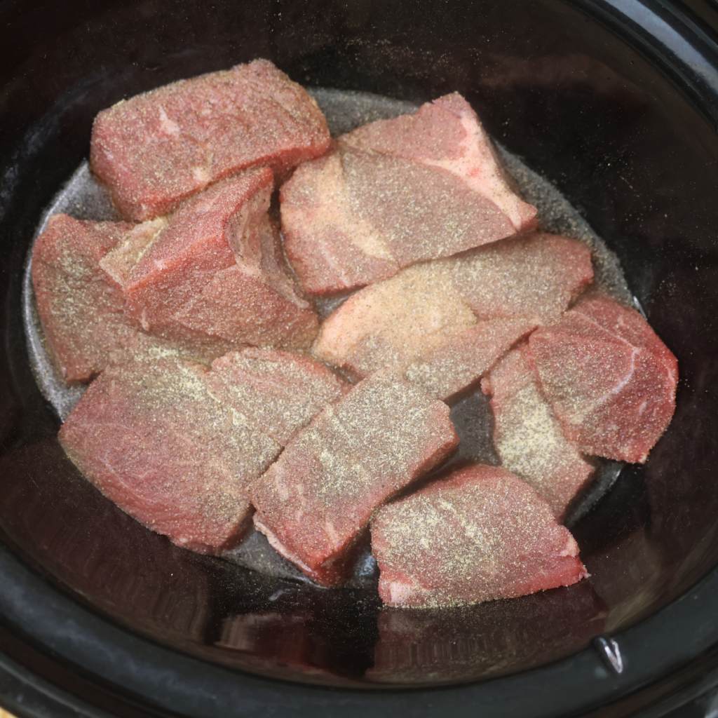 Chuck roast cut into pieces and seasoned in a slow cooker