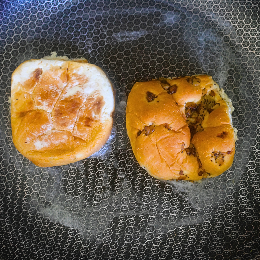 An onion roll being toasted in a skillet with butter